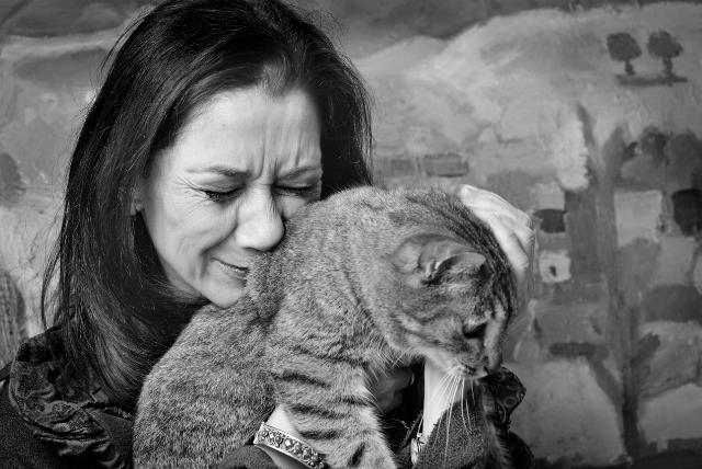 Black-and-white photo of a dark-haired female looking sad and holding her cat up to her face