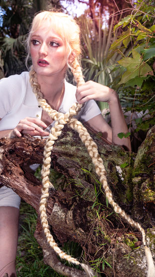 a woman with braided hair is sitting on a tree branch