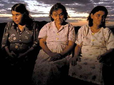 3 mulheres cegas, uma sentada ao lado da outra, e o por do sol por tras.