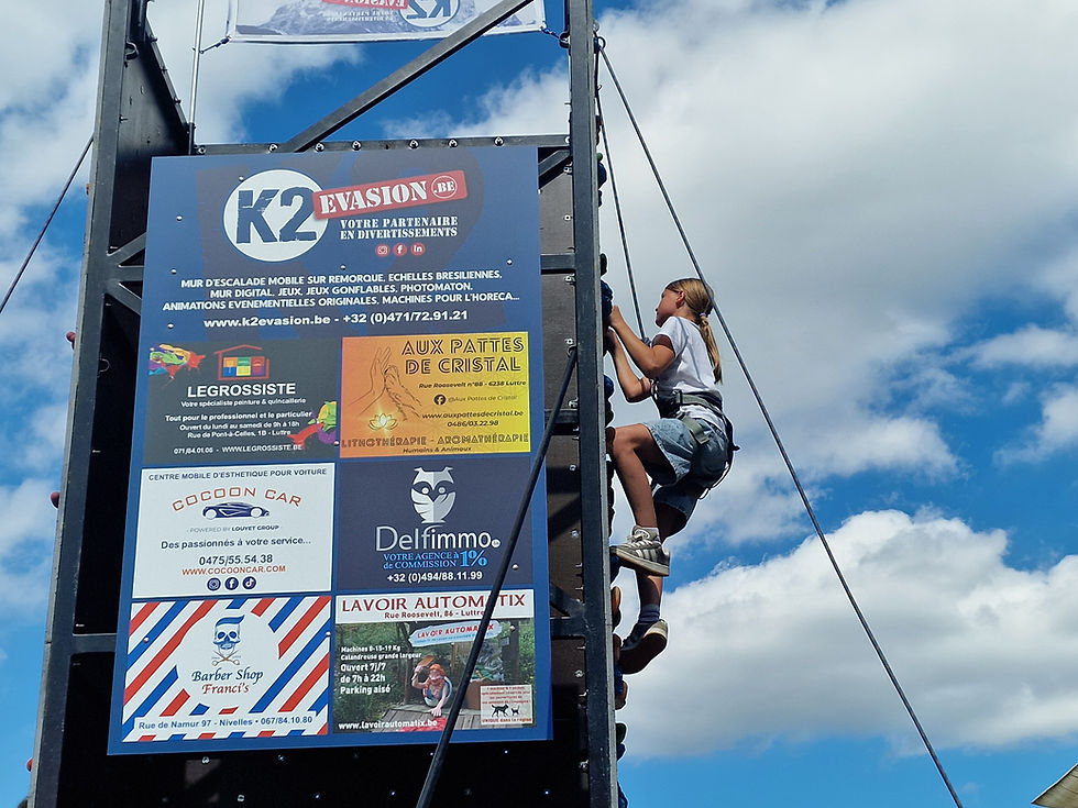 Le panneau publicitaire du mur d'escalade de K2Evasion lors de Louvain La Plage 2026 avec une grimpeuse motivée