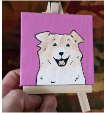 Small painted dog portrait on a tiny easel, held in a hand, with a pink background and a cheerful expression.