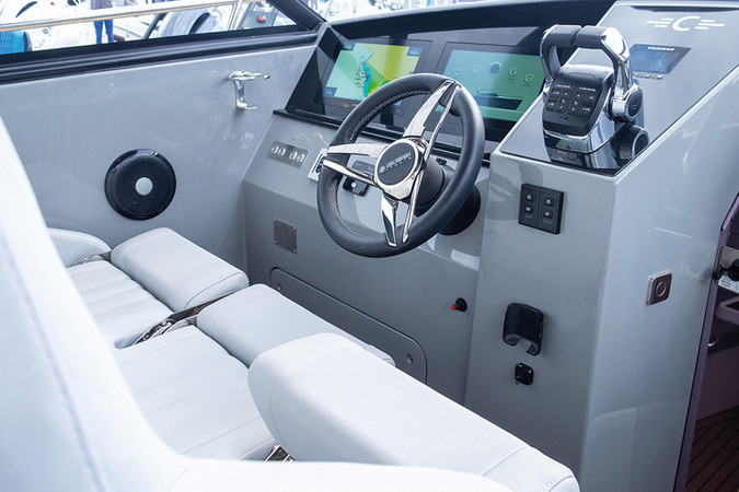 Modern boat helm with gray console, steering wheel, digital displays, throttle, and white cushioned seats.