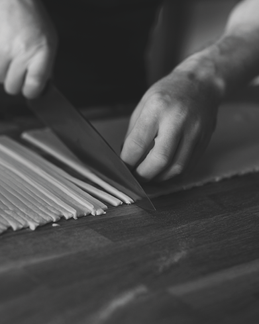  Black-and-white close-up of hands slicing thin white vegetables on a cutting board with a chef’s knife.