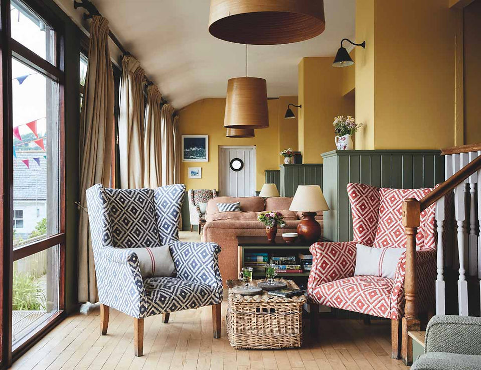 Cozy living room with patterned armchairs, sofa, wicker table, large windows, and warm yellow walls in a calm, inviting setting