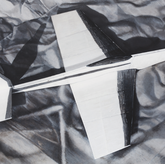 White model airplane with black accents resting on wrinkled dark fabric background, viewed from above.
