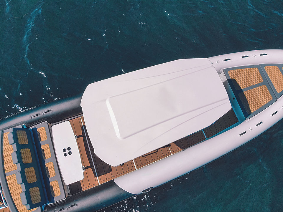 Top-down view of a white inflatable boat with tan-and-blue seats floating on dark water.