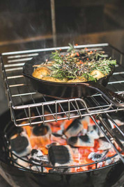 Cast-iron skillet of potatoes and rosemary roasting on a grill over glowing charcoal embers