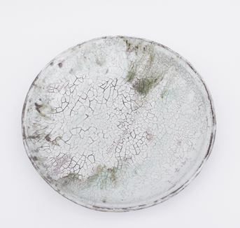 Cracked white ceramic plate with faint green and purple stains, centered on a plain white background