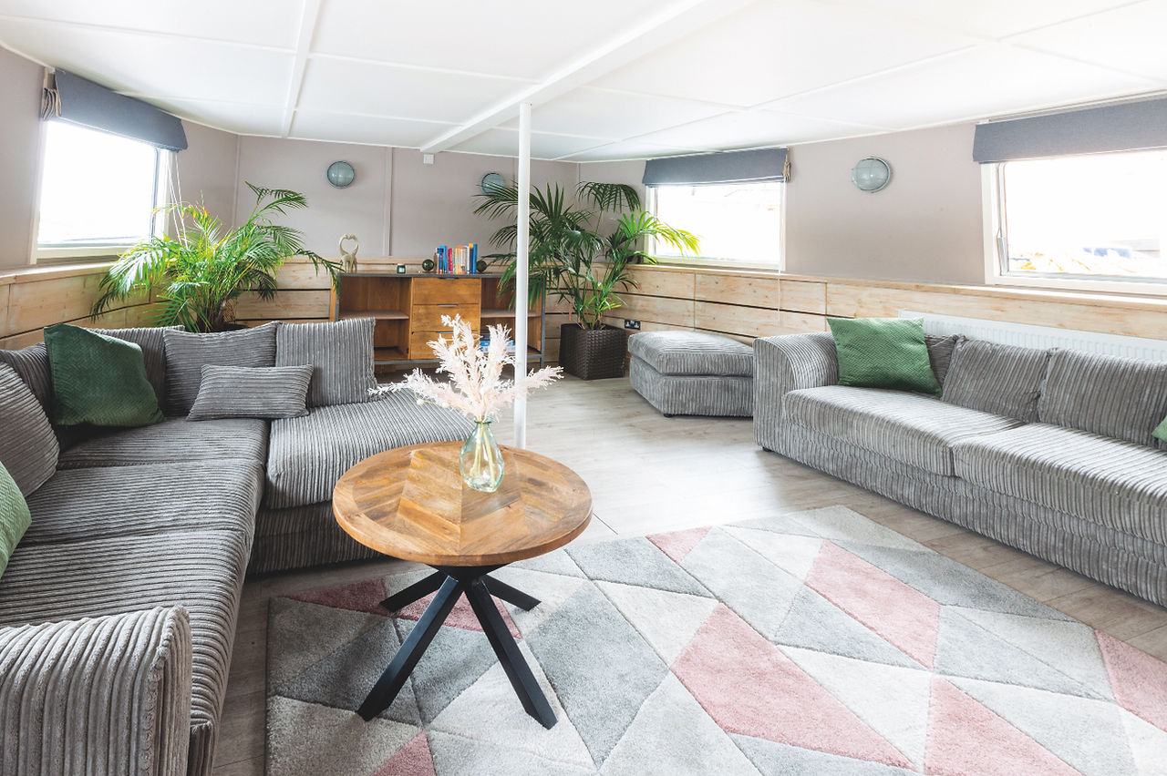 Bright modern lounge with gray sofas, wooden coffee table, potted palms, and pastel geometric rug in a sunlit room