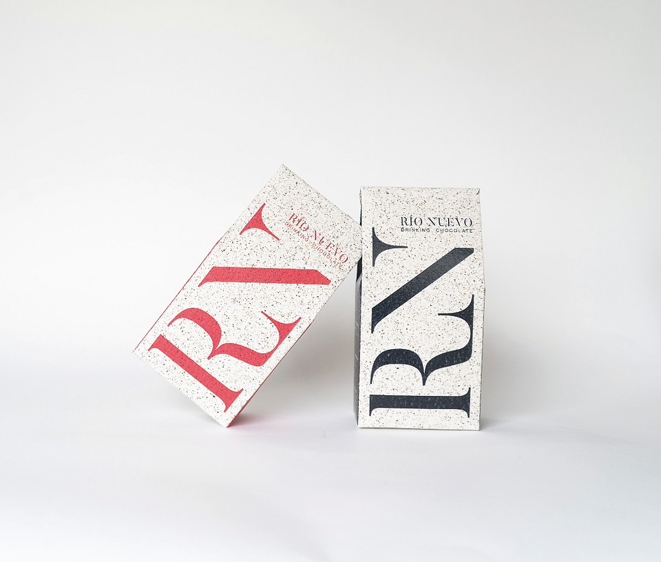 Two Rio Nuevo drinking chocolate boxes, one red leaning and one black upright, on a white studio background.