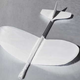 White model glider with taped black fuselage and tail on a gray surface, casting soft shadows.