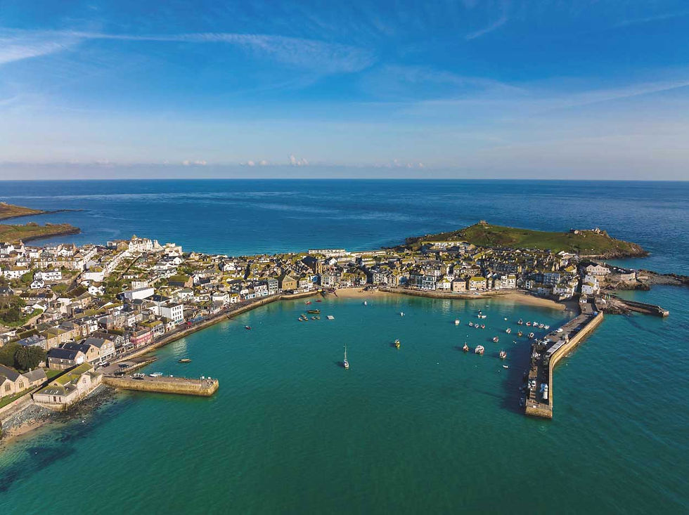 Aerial view of a coastal town and harbor with boats in turquoise water, stone piers, and a clear blue sky