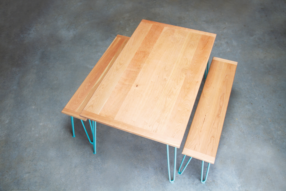 Wooden picnic table with two benches and turquoise metal legs on a gray concrete floor. Designs by Coast Creative