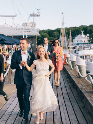 Smiling bride and groom walk hand-in-hand on a dock