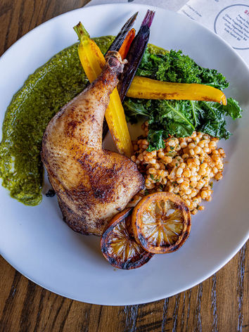 Roasted chicken leg with greens, grains, carrots, and lemon