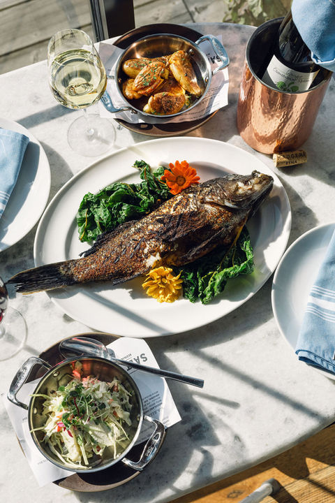 Grilled fish with greens, potatoes, and wine on a table