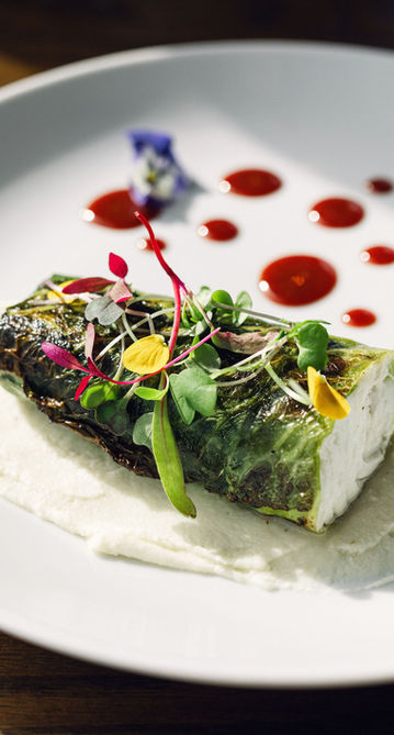 Gourmet food wrapped in green leaf with red sauce and flowers