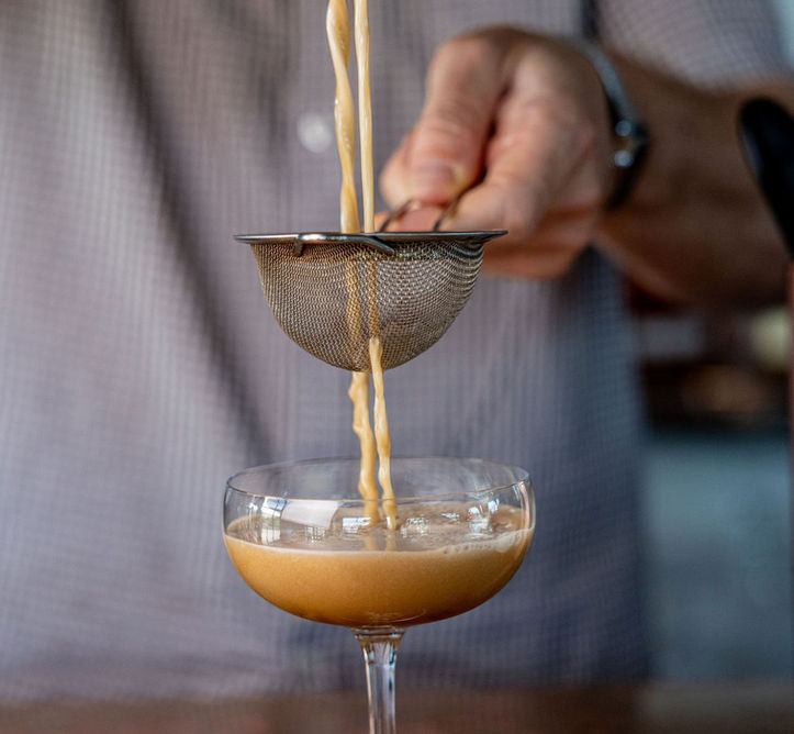 Person pouring cocktail from shaker into glass