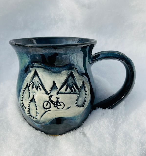 Black mug with green highlights and a picture of a bike riding through the mountains.