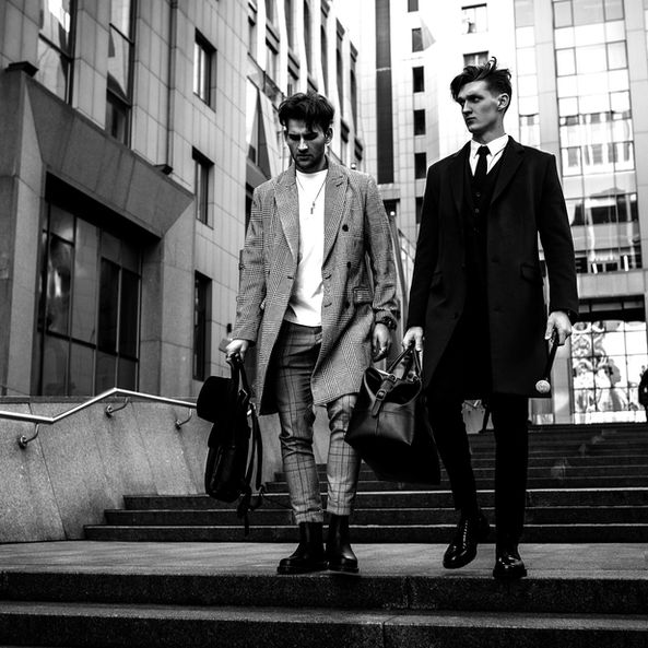 Two men in suits descend steps, urban backdrop