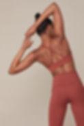 Femme en brassière et leggings terracotta s'étirant de dos