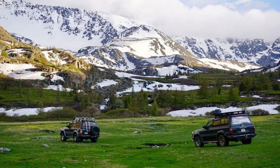 4×4 jeeps on a green meadow below snow-capped Altai mountains