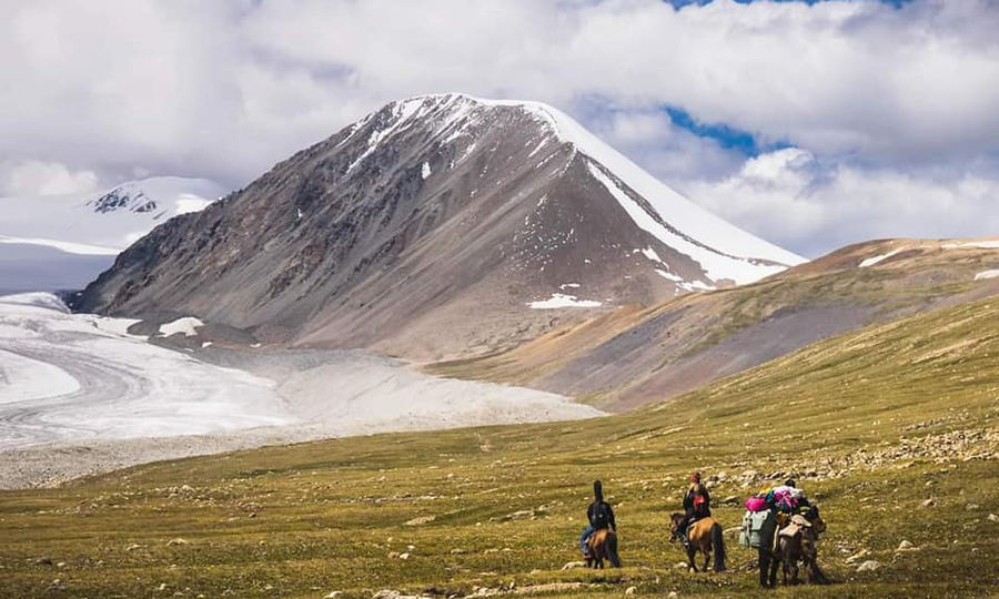 Horse riders below Potanin Glacier and the snowy Altai Tavan Bogd peaks