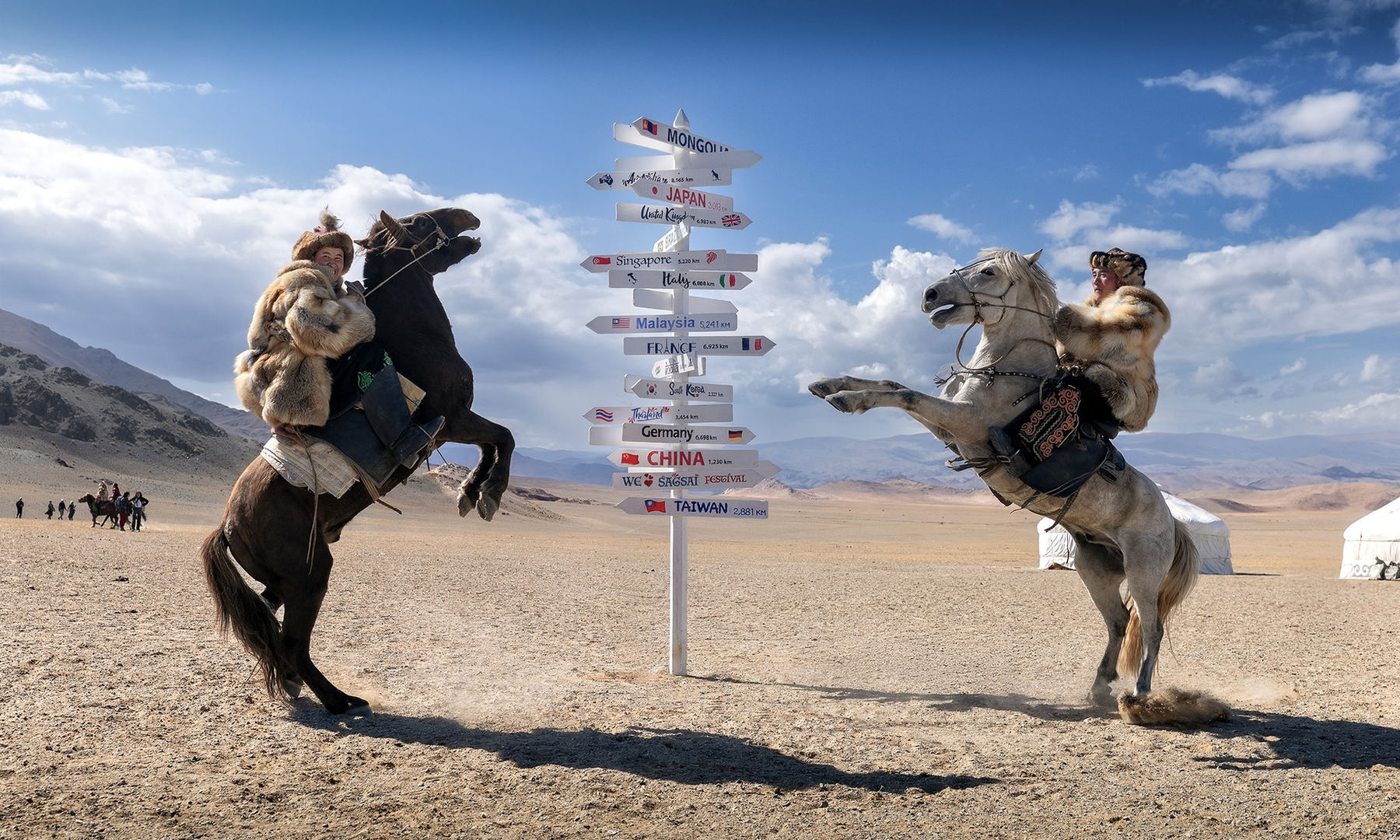 Two Kazakh eagle hunters on rearing horses beside a signpost in the Altai, western Mongolia