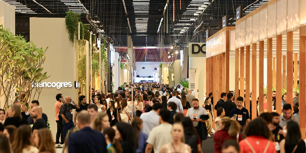 Corredor de feira ou evento corporativo lotado, com muitas pessoas circulando entre estandes modernos, iluminação profissional e estruturas de madeira, em um ambiente de networking e negócios.
