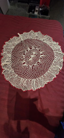 a white crocheted doily with a red border sits on a red cloth