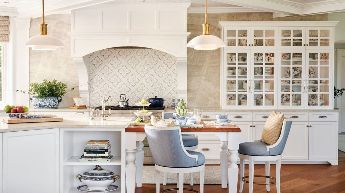 Luxury coastal kitchen with white shaker cabinets, quartz and wood countertops, large island, farmhouse sink, decorative white wood hood, intricate backsplash, and blue and white accents.