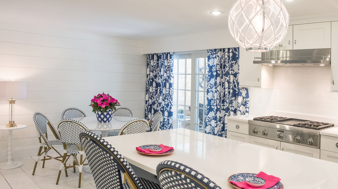 Large kitchen with a long blue shiplap island seating six, white quartz countertop, white shaker cabinets with wood accents, paneled dishwasher, and stainless steel hood over range.