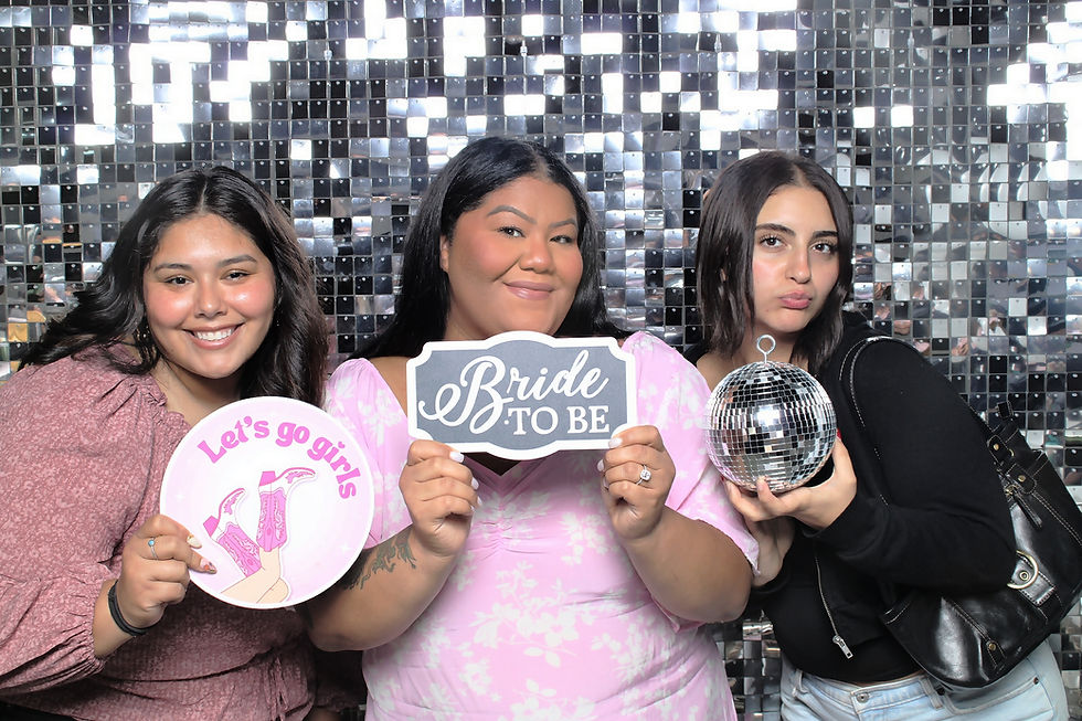 Three women pose in front of a mirrored backdrop. One holds a "Let's go girls" sign, another has a "Bride to be" sign, and the third holds a disco ball.