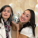 Two women smiling, holding disco ball, against a bokeh background. Captured Celebrations.
