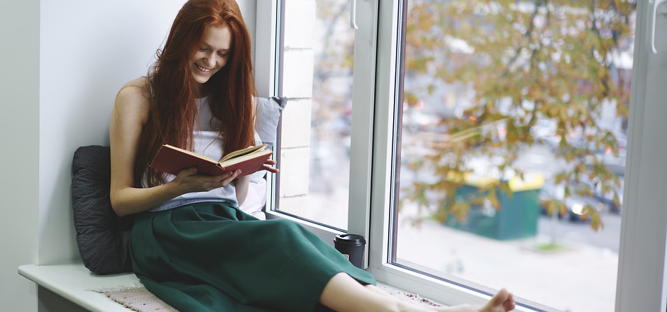 Cheerful beautiful foxy hipster girl reading funny poems in book relaxing during free time