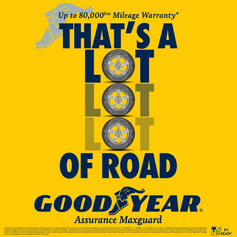 Promotional Goodyear advertisement featuring the headline "THAT'S A LOT LOT LOT OF ROAD", with three tyre images creatively replacing the letter "O" in the word "LOT." At the top, the ad highlights *"Up to 80,000km Mileage Warranty"**. The Goodyear logo appears prominently at the bottom above the product name Assurance MaxGuard, with an EV Ready badge in the lower-right corner. The design uses Goodyear's signature yellow background with bold navy typography, emphasizing durability, long-lasting performance, and mileage warranty. Fine print with warranty terms is displayed along the bottom edge.