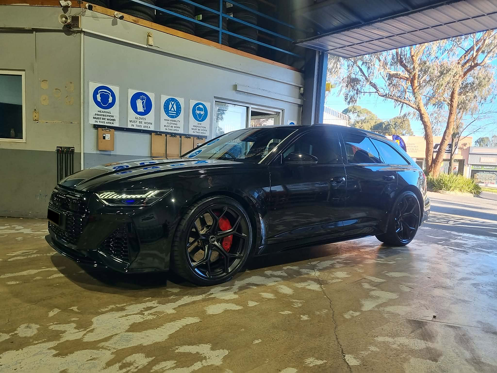 A black Audi RS6 Avant with red brake calipers parked inside a workshop garage bay after their tyres have been changed
