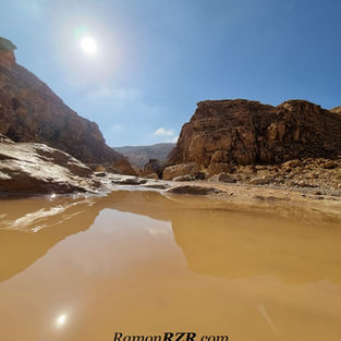 רייזר רמון | טיול מכתש רמון | חוויה במדבר | פרסת נקרות | השתקפות של מצוקי המדבר והשמש בתוך שלולית מים צלולה בלב קניון סלעי.