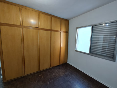 Quarto vazio com piso de madeira, paredes brancas e janela deixando entrar luz natural.