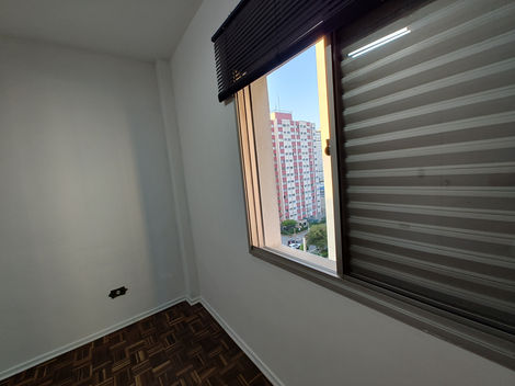Quarto vazio com piso de madeira, paredes brancas e janela deixando entrar luz natural.
