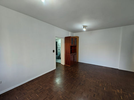 Quarto vazio com piso de madeira, paredes brancas e janela deixando entrar luz natural.