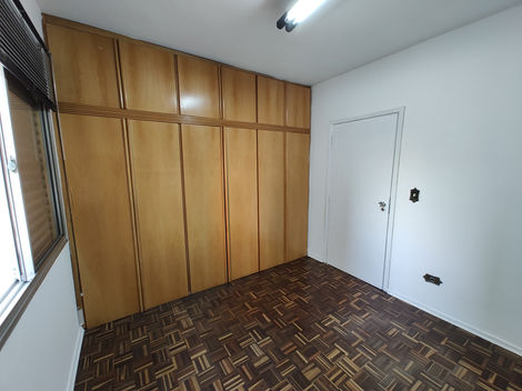 Quarto vazio com piso de madeira, paredes brancas e janela deixando entrar luz natural.