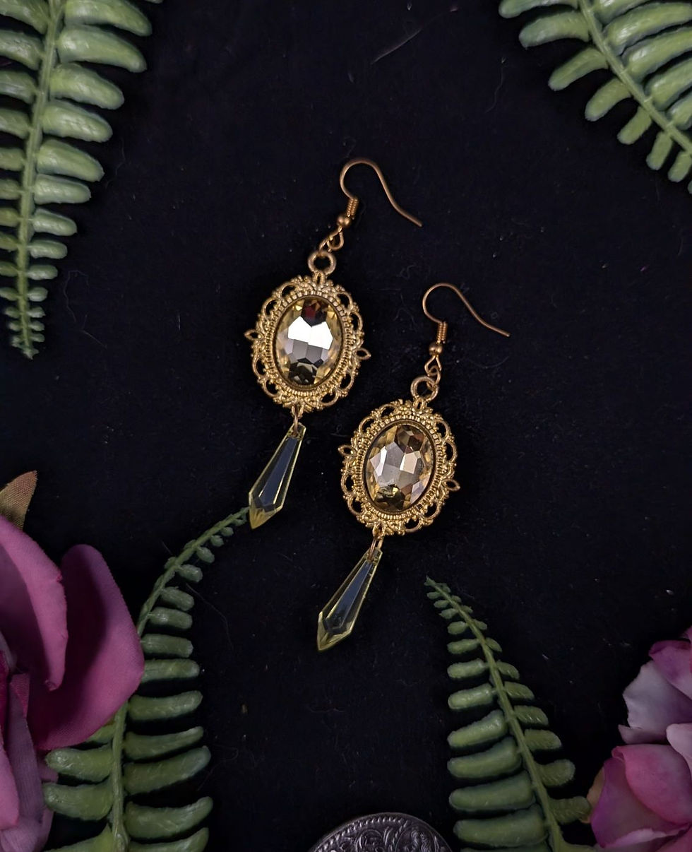 Goldene Ohrringe mit klaren Steinen, umgeben von Farn und Blumen auf Schwarz