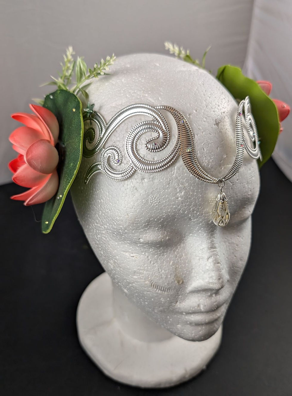 Silbernes Diadem mit rosa Blüten, grünen Sukkulenten auf Schaufensterpuppenkopf.