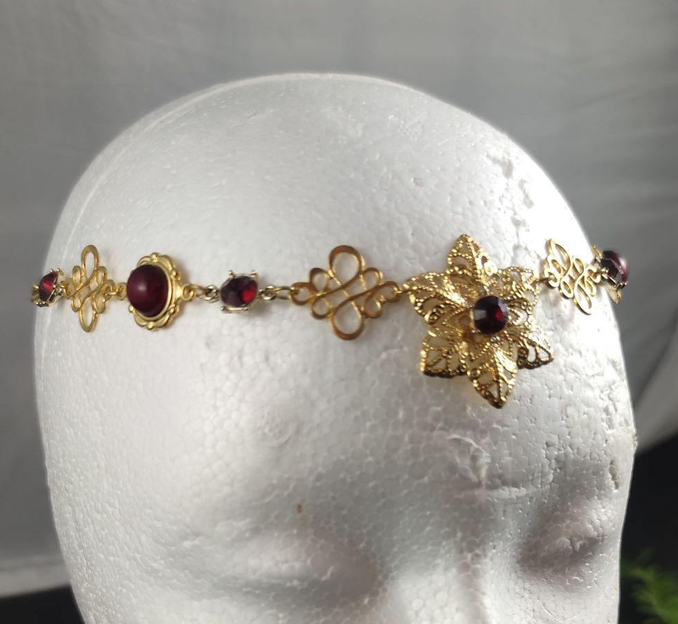 Goldener Stirnreif mit roten Edelsteinen und Blumenmuster auf weißem Kopf.