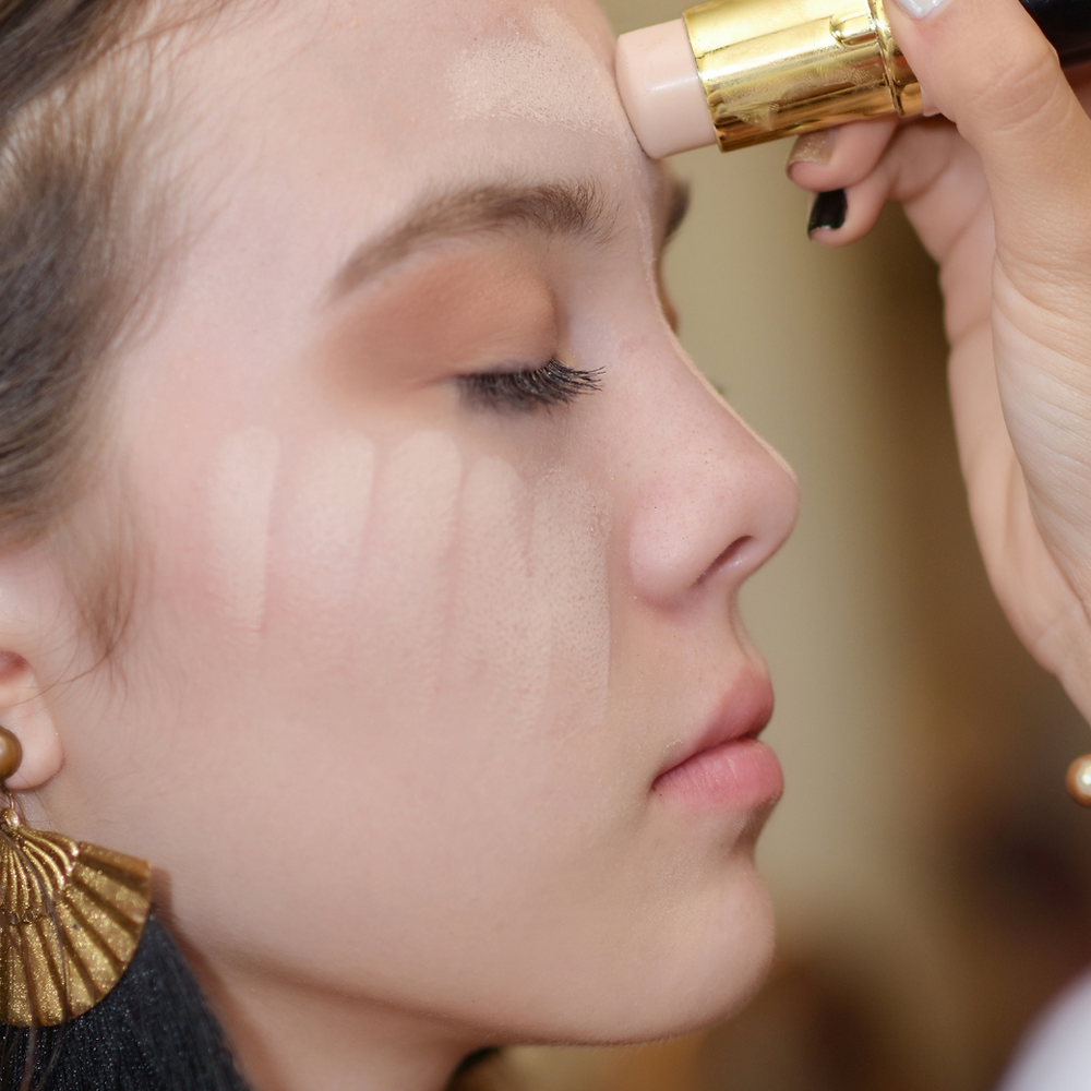 Perfil feminino de olhos fechados mostrando a aplicação de um corretivo em bastão