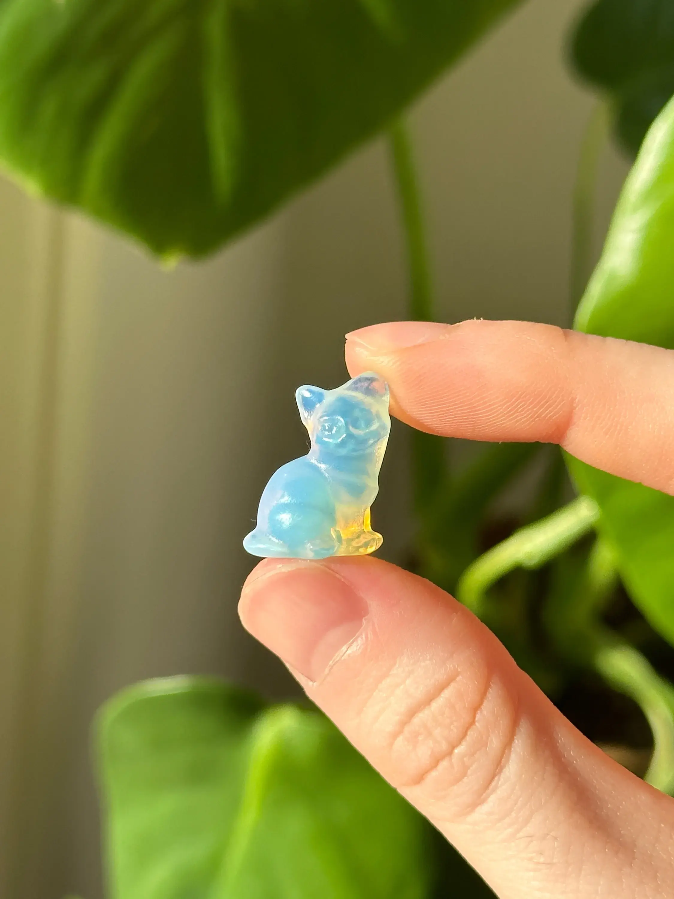 Hand holding an opalite cat carving with rainbow glow