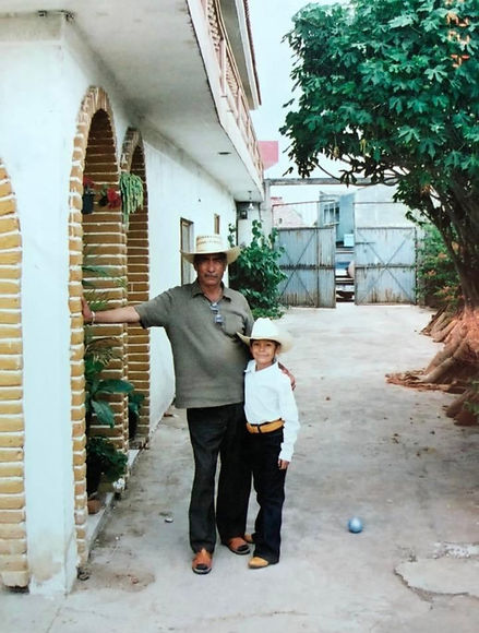 Nicole as a child wearing a sombrero and boots is hugging her abuelito, both facing and looking at the camera.