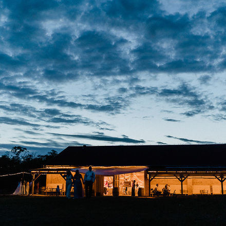 Nasvícená budova Stodola v meruňkovém sadu během svatebního večera pod dramatickou modrou oblohou uprostřed přírody.
