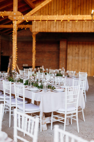 Interiér svatebního místa Stodola v meruňkovém sadu s přiznanými dřevěnými trámy, světelnými řetězy a prostřenými stoly pro hosty.